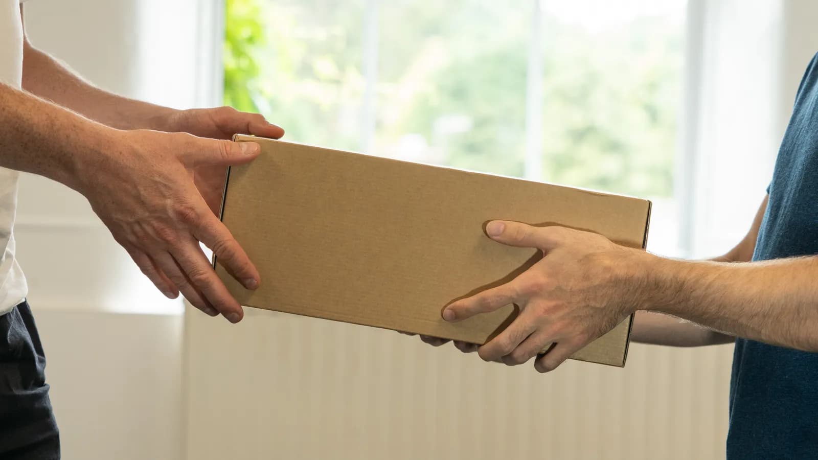 Zwei Hände übergeben einen Versandkarton an zwei andere Hände